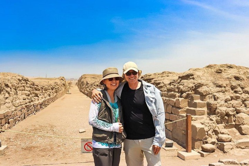 Twee personen staan in een archeologisch gebied met stenen muren en een heldere lucht. 4