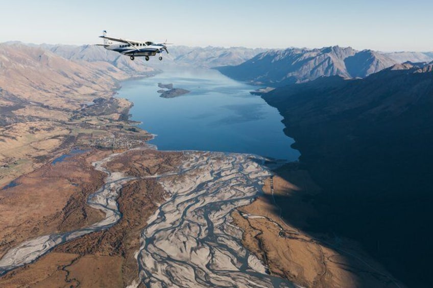 A small airplane flying over a mountainous landscape with a river and a lake. 2