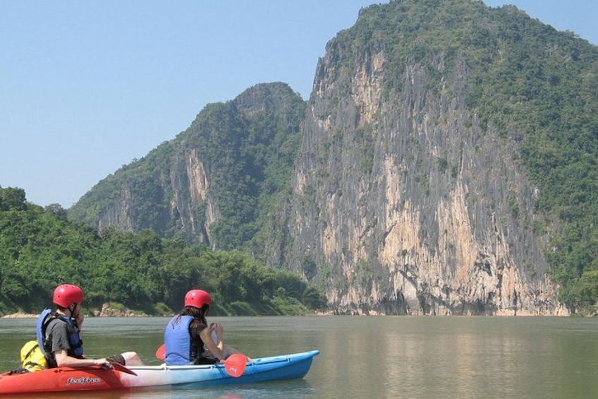 Two people kayaking on a calm river with a large mountain in the background. 1