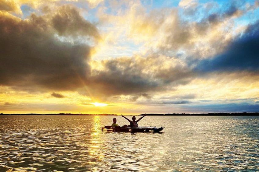 Ein Sonnenuntergang über einem Gewässer mit zwei Personen in einem Boot. 5