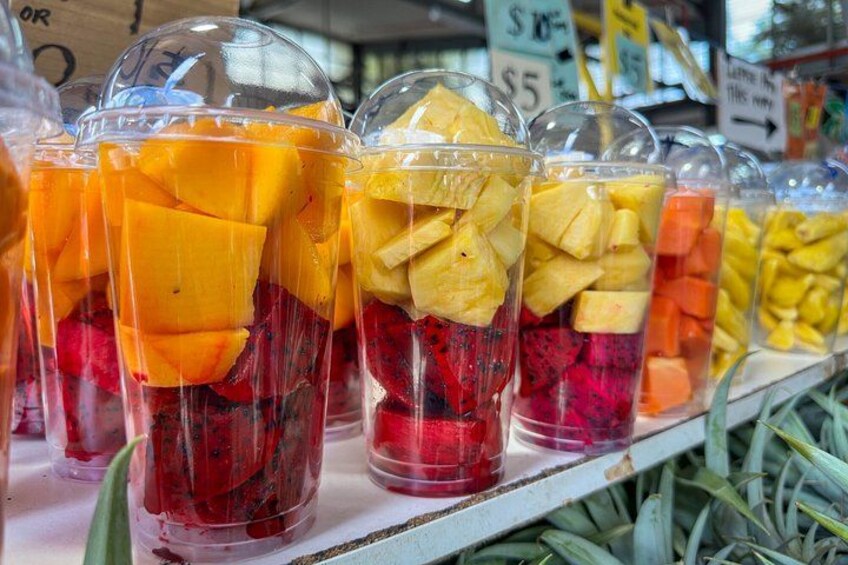 A display of fruit cups with clear lids, containing various fruits like mango and berries, priced at $5. 4