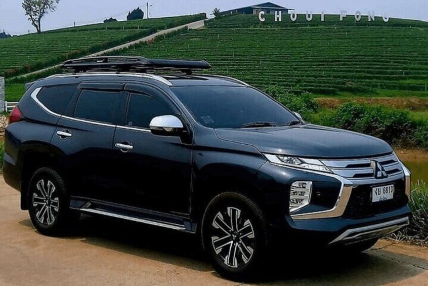 A dark-colored SUV parked on a dirt road with a green field and a hill in the background. 4