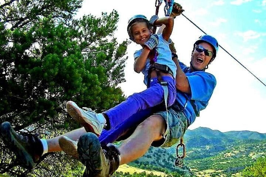 A person zip-lining with a child, surrounded by trees and a mountainous landscape. 3
