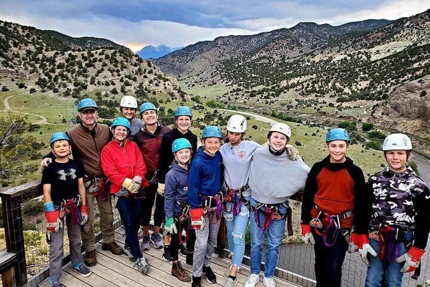 A group of people on a wooden platform with helmets and harnesses, overlooking a mountainous landscape. 4