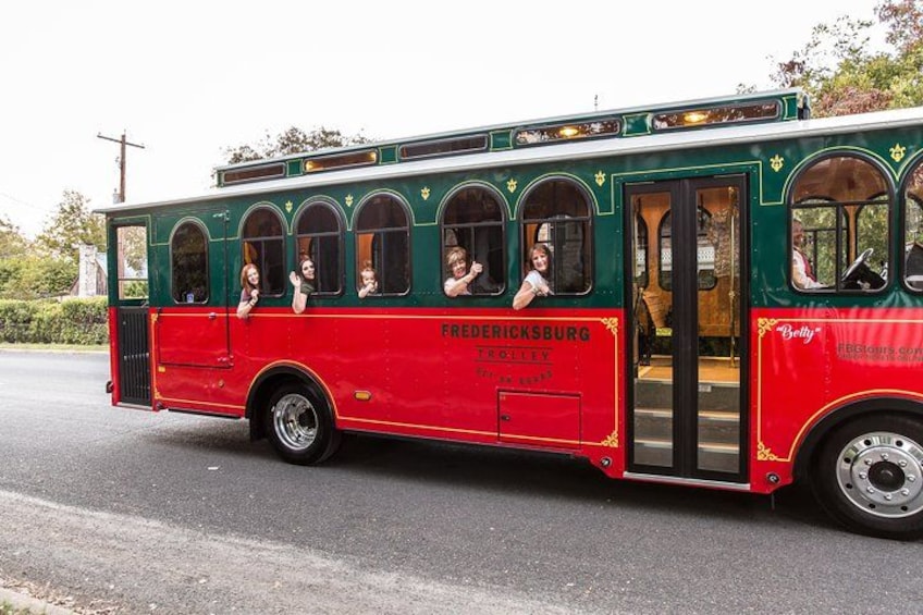 Ein roter und grüner Trolley mit Fahrgästen, beschriftet mit 'FREDERICKSBURG', auf einer Straße. 1