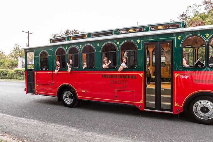 A vintage red and green trolley with passengers, labeled 'FREDERICKSBURG.' 1