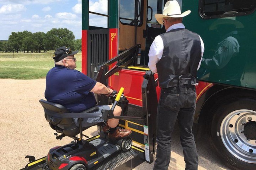 A person in a wheelchair next to a green bus, with a man standing beside them. 4