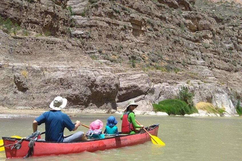 A group of people in a red canoe on a river with rocky cliffs in the background. 4
