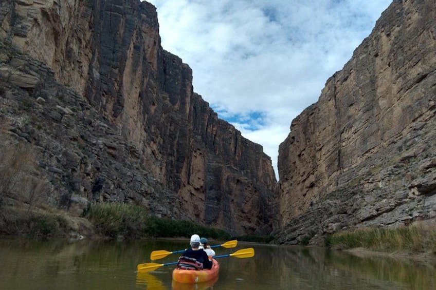 A kayaker paddling through a canyon with steep rock walls. 1