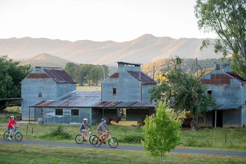 Three cyclists on a road with old buildings and mountains in the background. 4