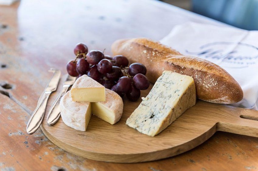 A wooden cutting board with various cheeses, grapes, and a baguette on a rustic table. 5