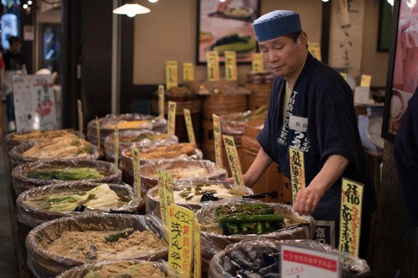 A person in traditional attire at a food stall with various food items and price tags. 3