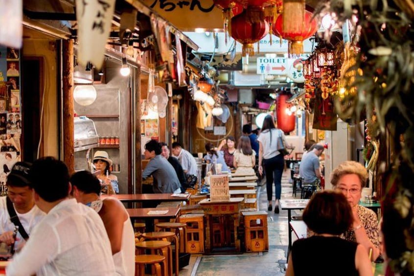 A bustling indoor market with wooden tables, red lanterns, and signs in a foreign language. 1