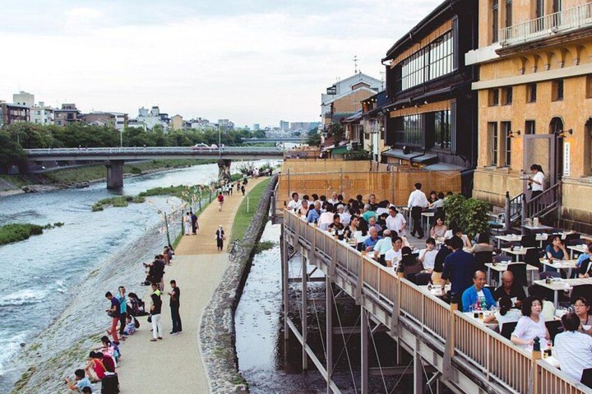 A riverside walkway with people walking and dining on a bridge. 4