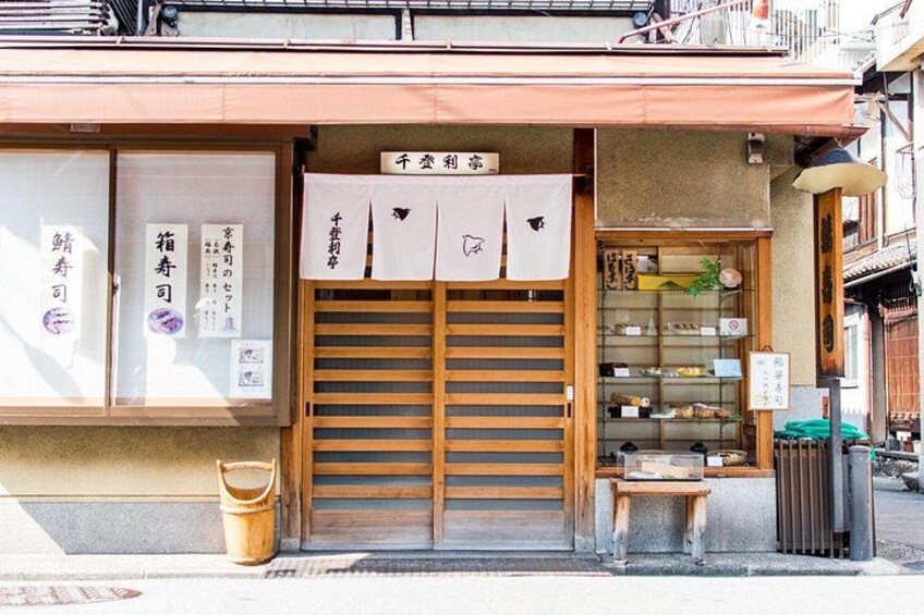 A traditional Japanese shop with wooden shutters, a signboard, and a small stool outside. 2