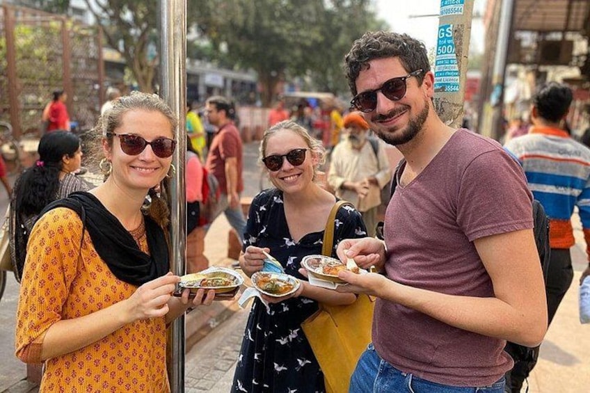 Three people eating at an outdoor food stall. 3