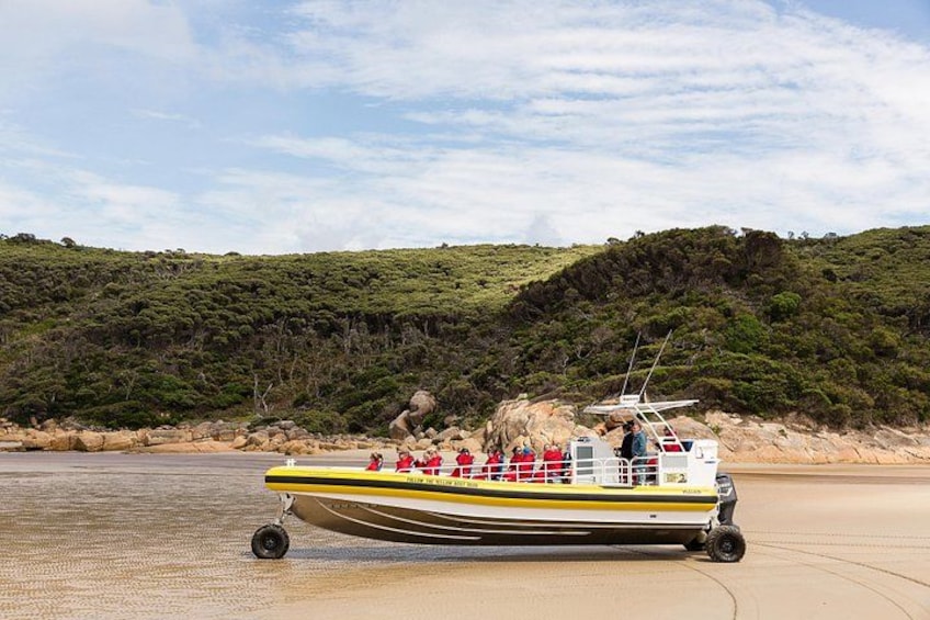 A boat on a sandy beach with a forested hill in the background. 5