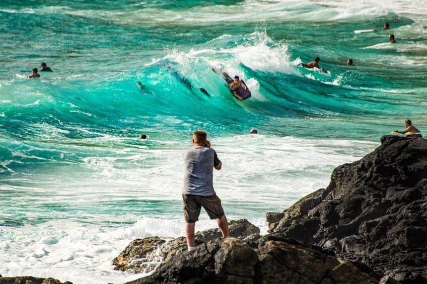 Un surfista montando una ola, gente nadando y un litoral rocoso. 2