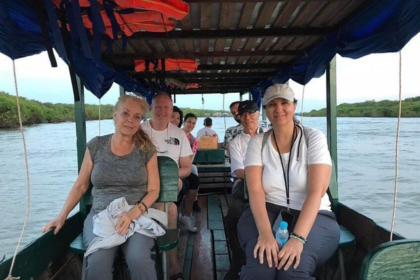 A group of people on a boat with a covered deck, surrounded by water and greenery. 4