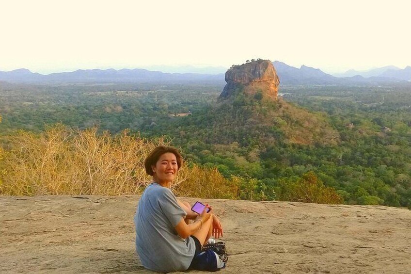 A person sitting on a sandy ledge overlooking a landscape with a prominent rock formation. 1