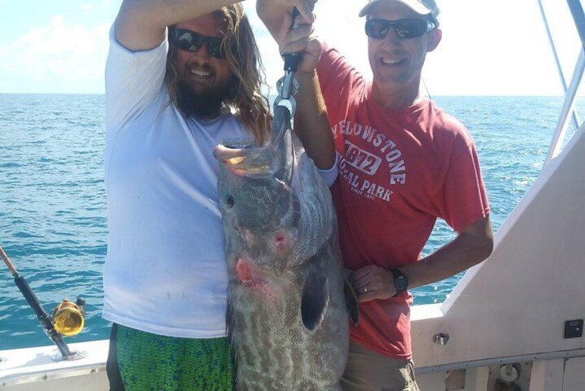 Two people on a boat holding a large fish. 4