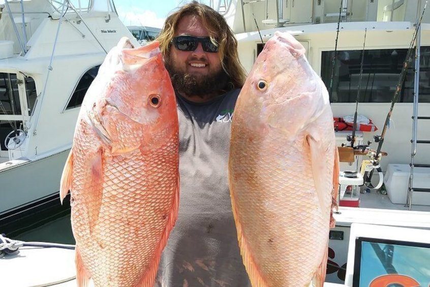 A person holding two large pink fish on a boat. 2