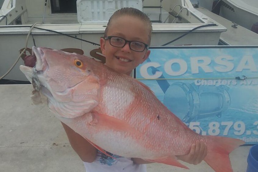 A person holding a large fish with a sign in the background. 3