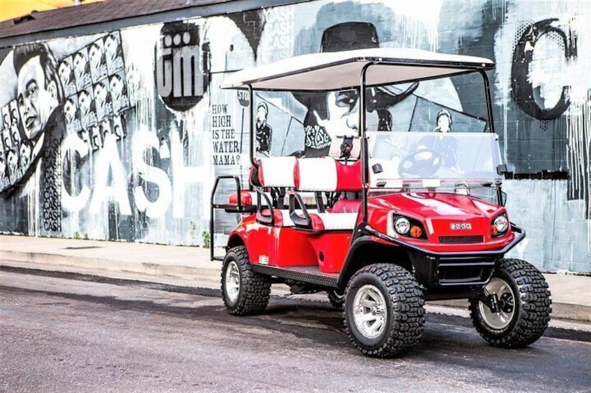 A red golf cart parked on a street with a mural in the background. 1