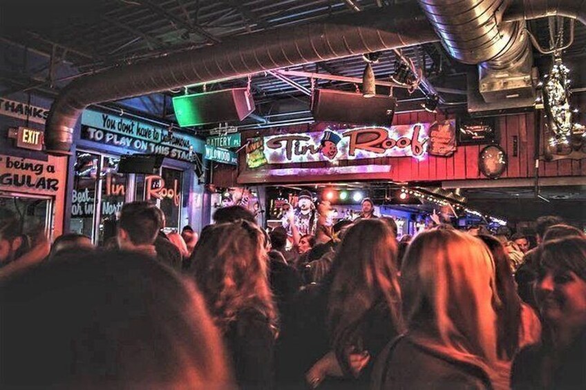 A crowded bar with neon signs and a stage. 3