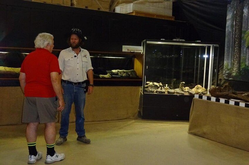 Two people standing in a room with a glass display case containing a model of a dinosaur habitat. 2