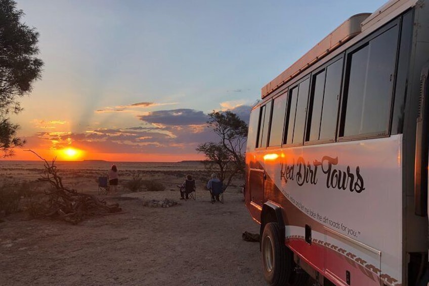 A bus with 'Red Dirt Tours' written on it parked on a beach at sunset. 4