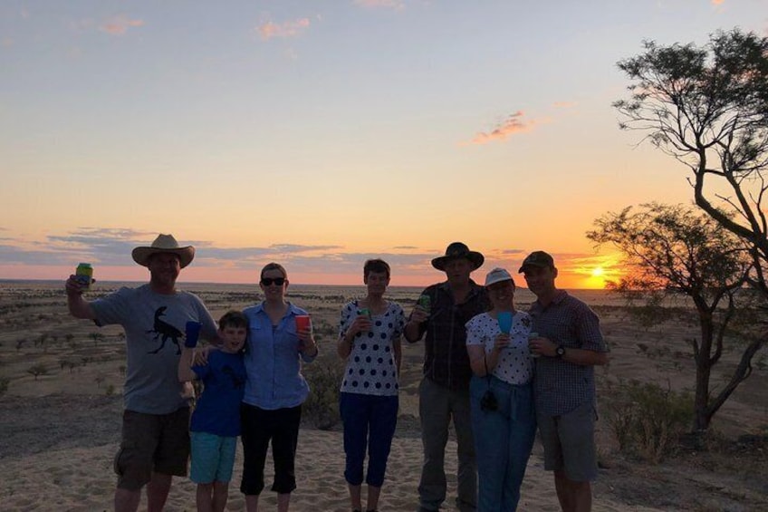 A group of people standing on a sandy terrain with a sunset in the background. 3