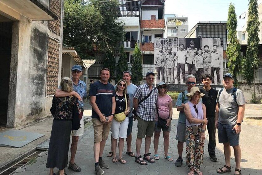 Un groupe de personnes se tient dans un espace extérieur, avec une fresque murale en arrière-plan. 4