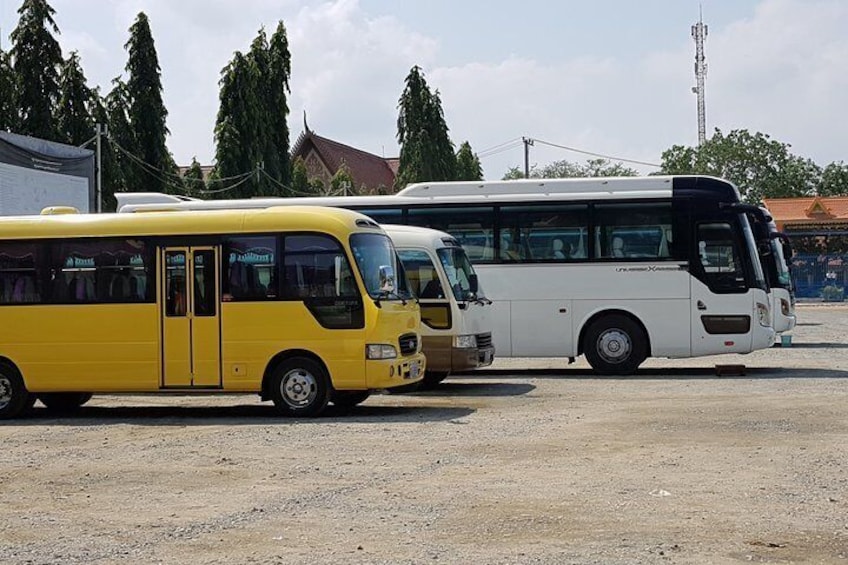 Two buses parked on a gravel surface with buildings and trees in the background. 4