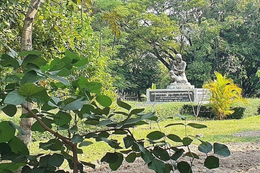 A statue in a park with lush greenery and a sign in the background. 2