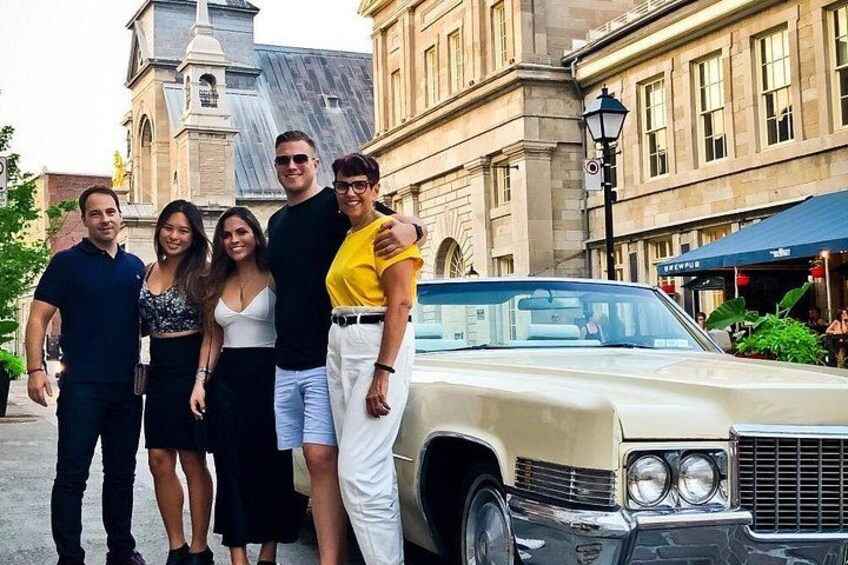 A group of people posing in front of a vintage car with a historic building in the background. 4