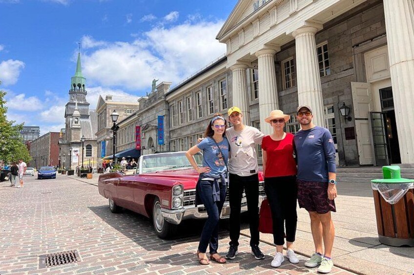 A group of people posing in front of a historic building with a classic car parked nearby. 3