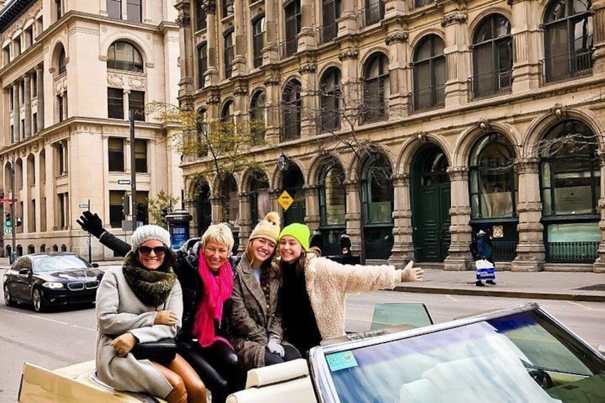Een groep mensen zit op een auto voor een historisch gebouw met boogvensters en een stenen gevel. 3