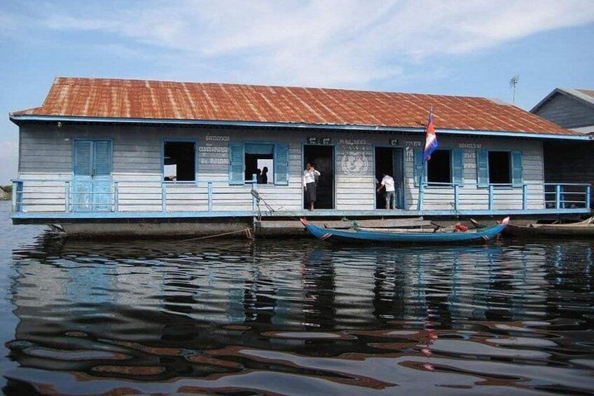 A houseboat with a blue exterior and a red roof, docked on calm water. 1