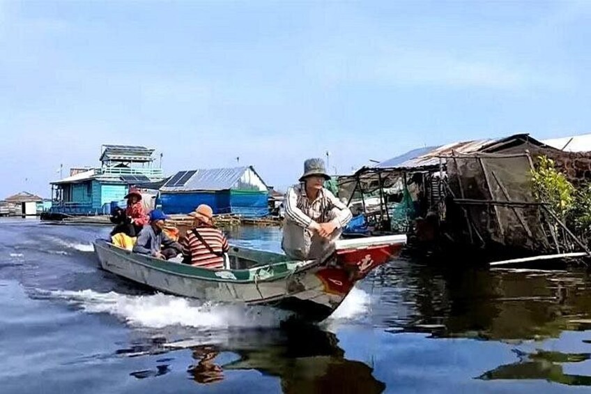 A boat with people on a calm water body, surrounded by floating structures and buildings. 3