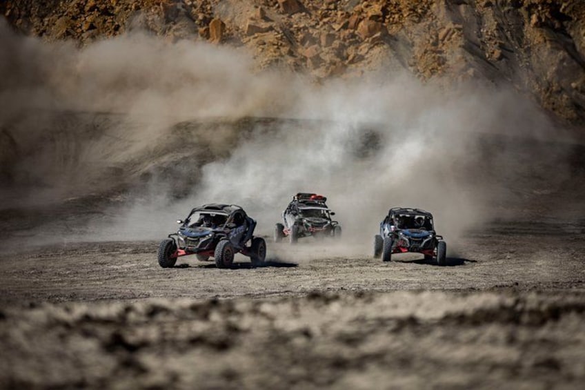 Three off-road vehicles racing on a dusty track with a rocky background. 4