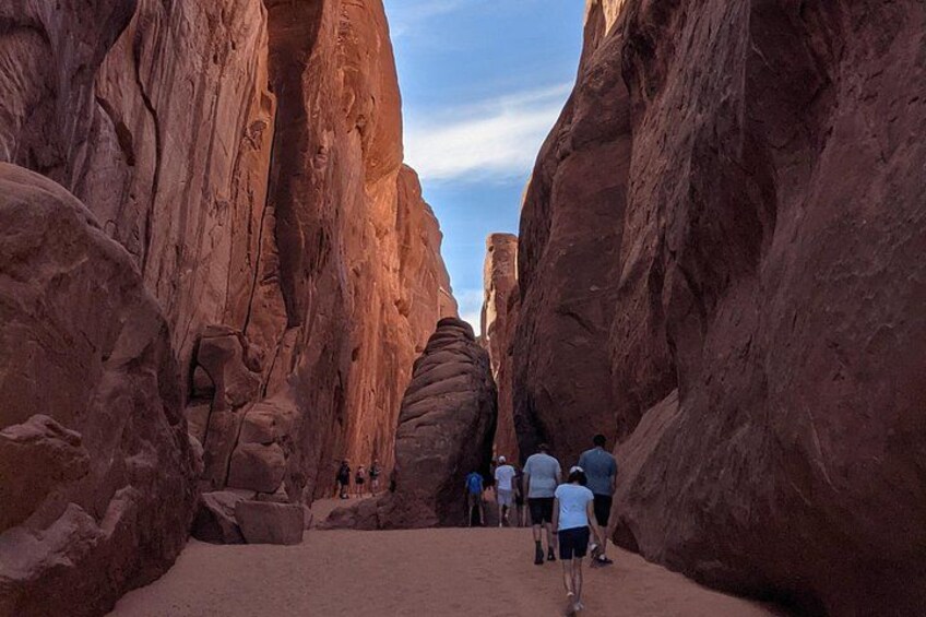 A narrow canyon with red rock walls and a group of people hiking. 1