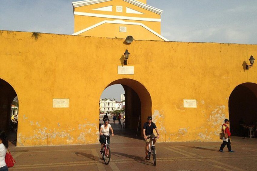A yellow wall with arches, a person on a bicycle, and another person walking. 4