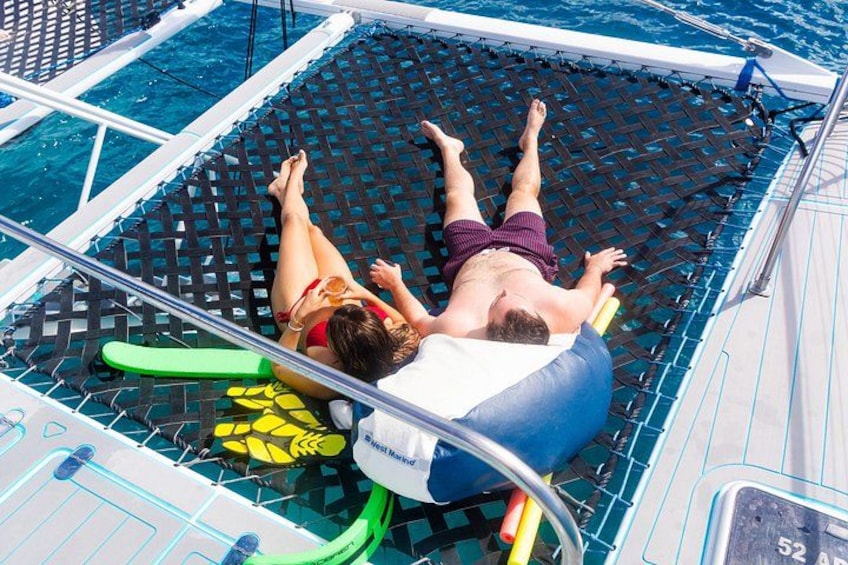 Two people lying on a floating platform in a body of water, surrounded by a pool and a boat deck. 2