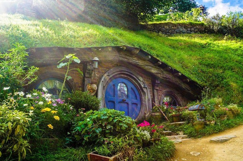 A Hobbit-style house with a blue door, surrounded by lush greenery and flowers. 1