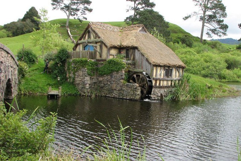 A thatched-roof house with a water wheel by a river. 4