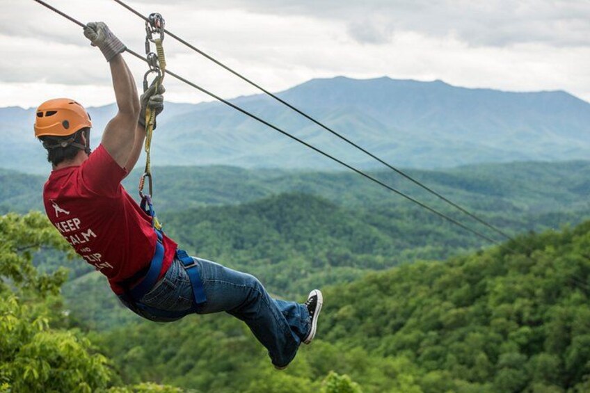 En person åker på en zipline över ett bergigt landskap. 3
