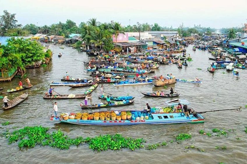 A bustling river with numerous boats, some carrying goods, surrounded by greenery and buildings. 2