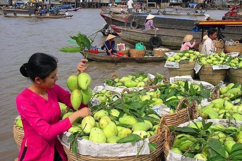 A woman in a pink shirt holding a bunch of green coconuts, with baskets of coconuts and boats in the background. 3