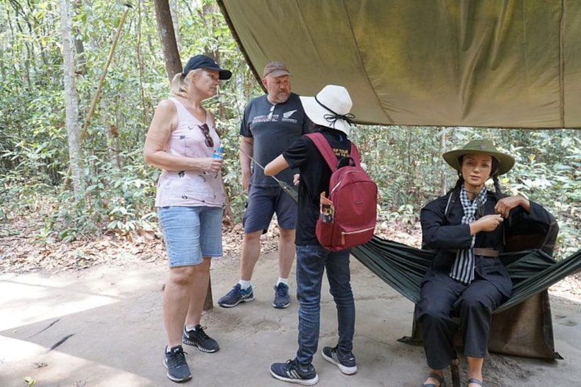 A group of people sitting and standing under a canopy in a wooded area. 4